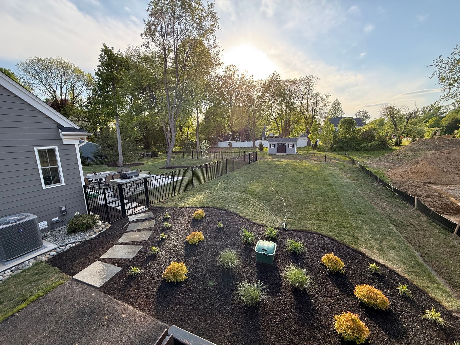 Backyard garden with flower beds, patio stones, and trees at sunset
