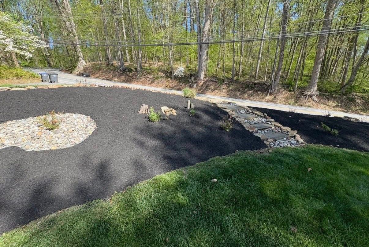 Landscaped yard with black mulch beds, stepping stones, and trees along a wooded edge