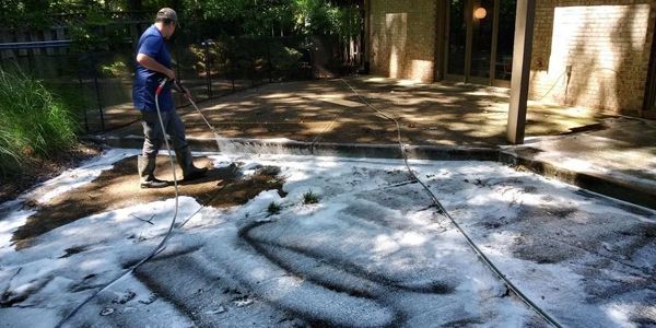 a man is applying biodegradable detergent to a concrete patio with a pressure washing machine in McLean, Virginia