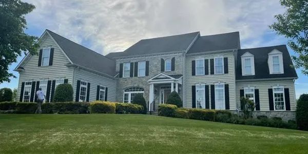 Pressure Washing results for a large white house with a black roof is sitting on top of a lush green hillside in Lorton, Virginia