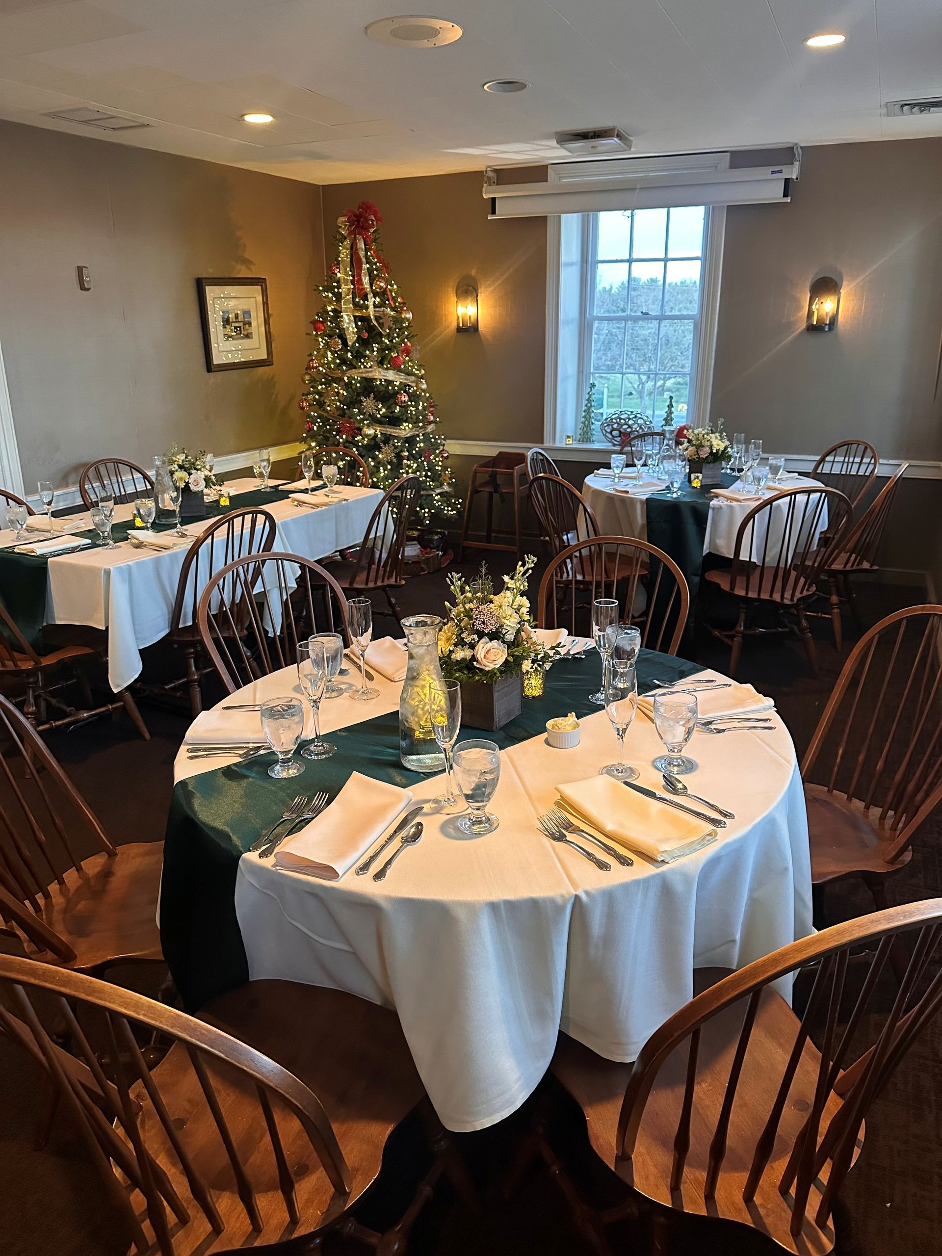 A dining room with tables and chairs and a christmas tree in the background.