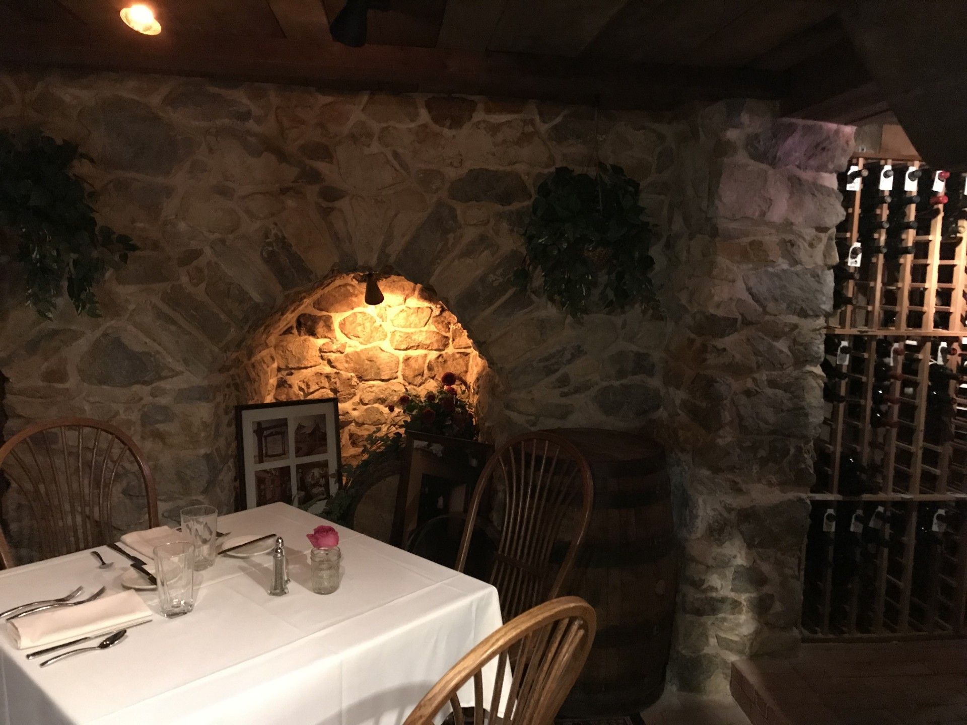 Stone-walled restaurant dining nook with white tablecloth table, chairs, and wine rack by the wall lamp