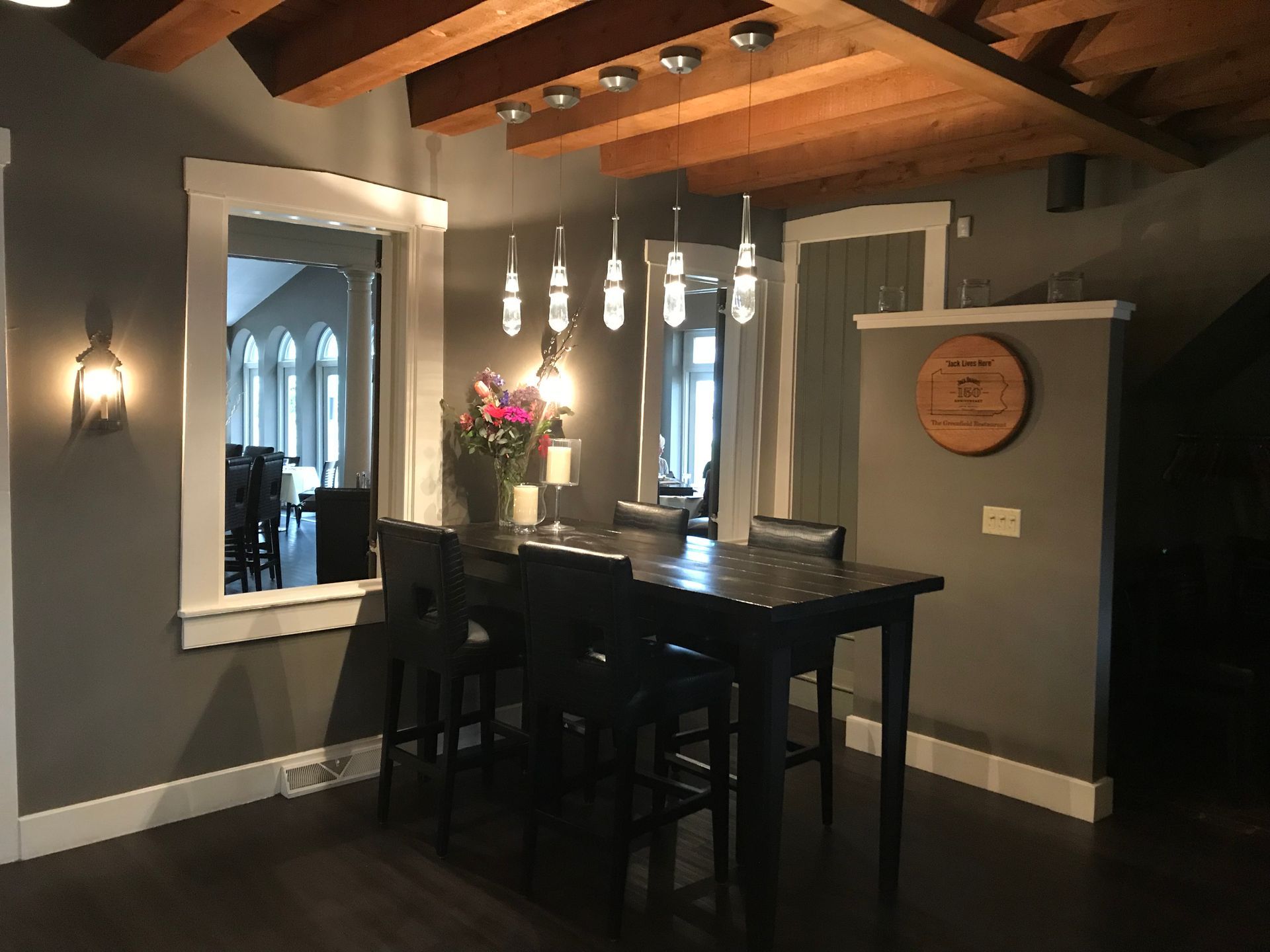 Cozy dining nook with a dark table and stools, pendant lights, and arched window mirrors in gray-brown tones