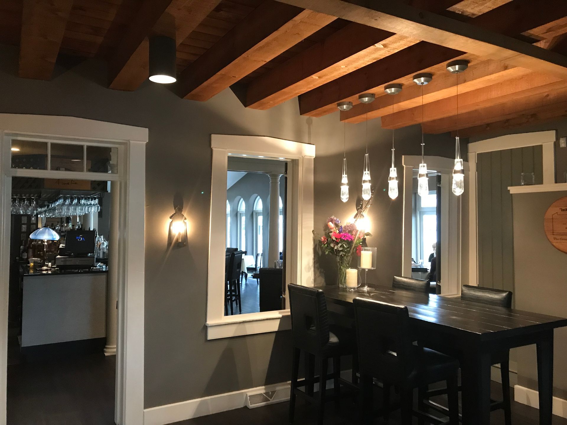 Cozy dining room with exposed wood beams, pendant lights, and a black table beside large windows.