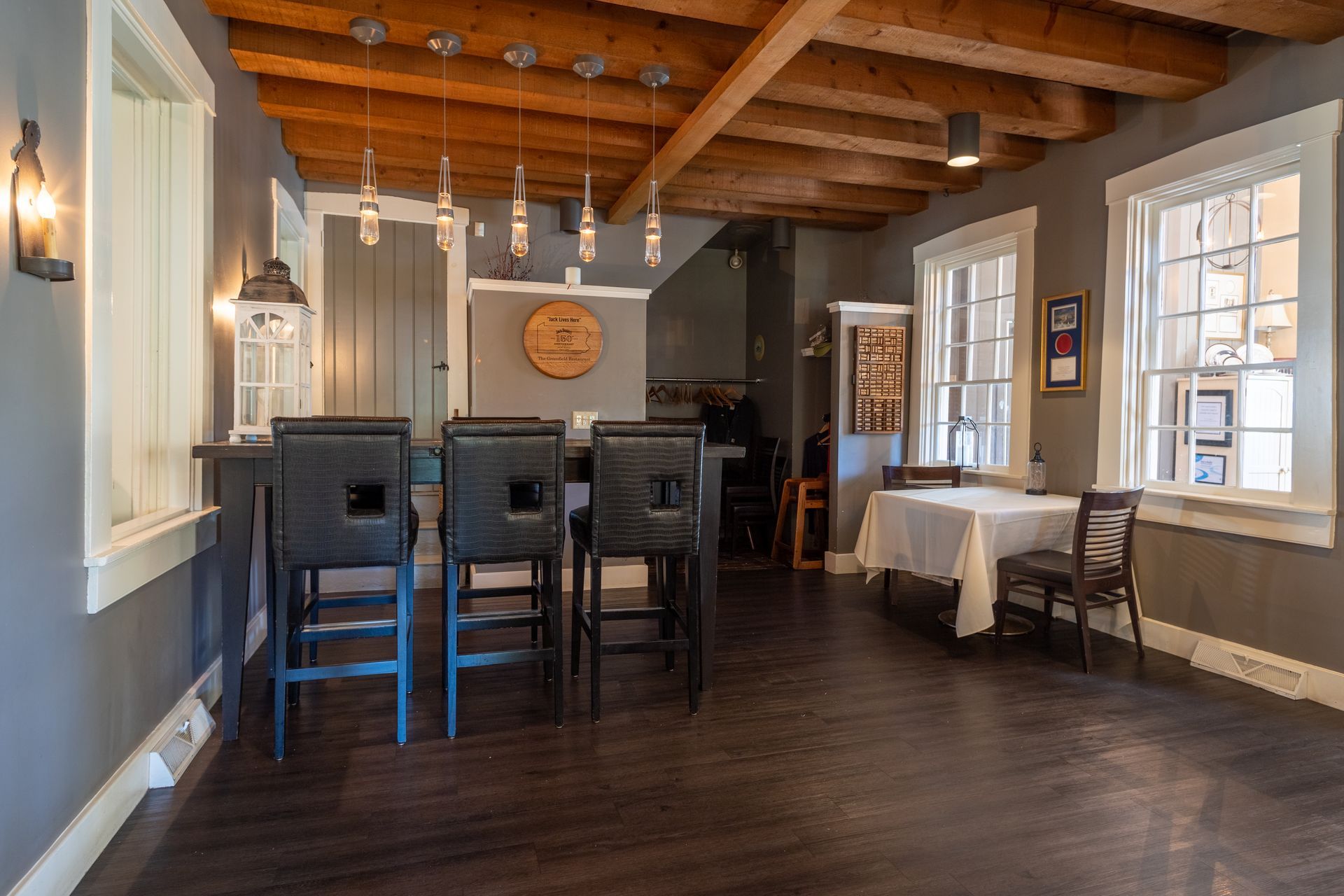 Cozy dining room with wooden beams, dark table and chairs, pendant lights, and a windowed wall