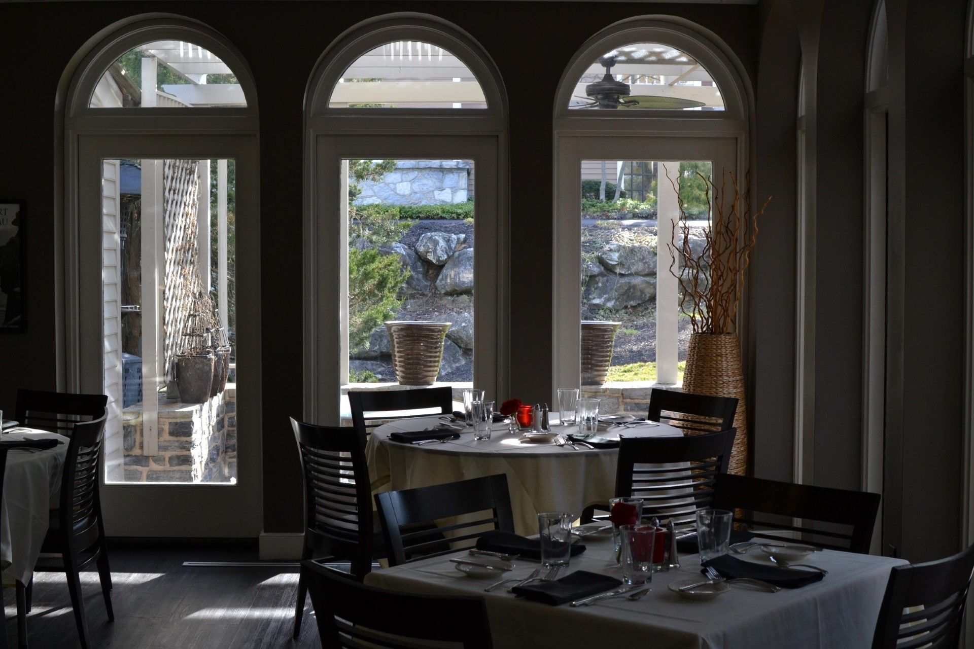 Dim restaurant dining room with arched windows overlooking a courtyard fountain.