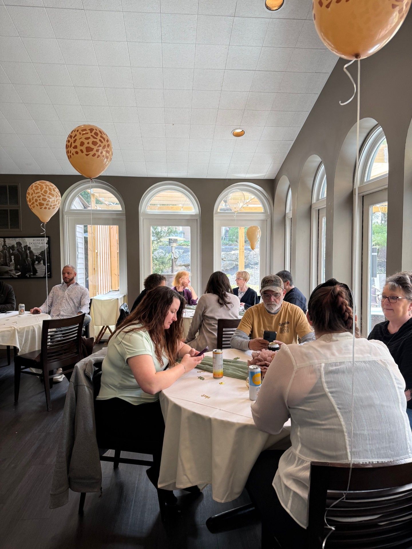 People seated at round tables in a bright cafe with arched windows and hanging balloons