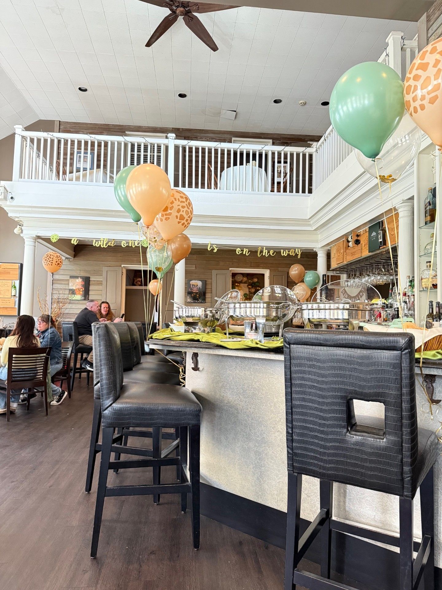 Balloons over a café bar with stools, tables, and patrons in a bright, airy restaurant interior