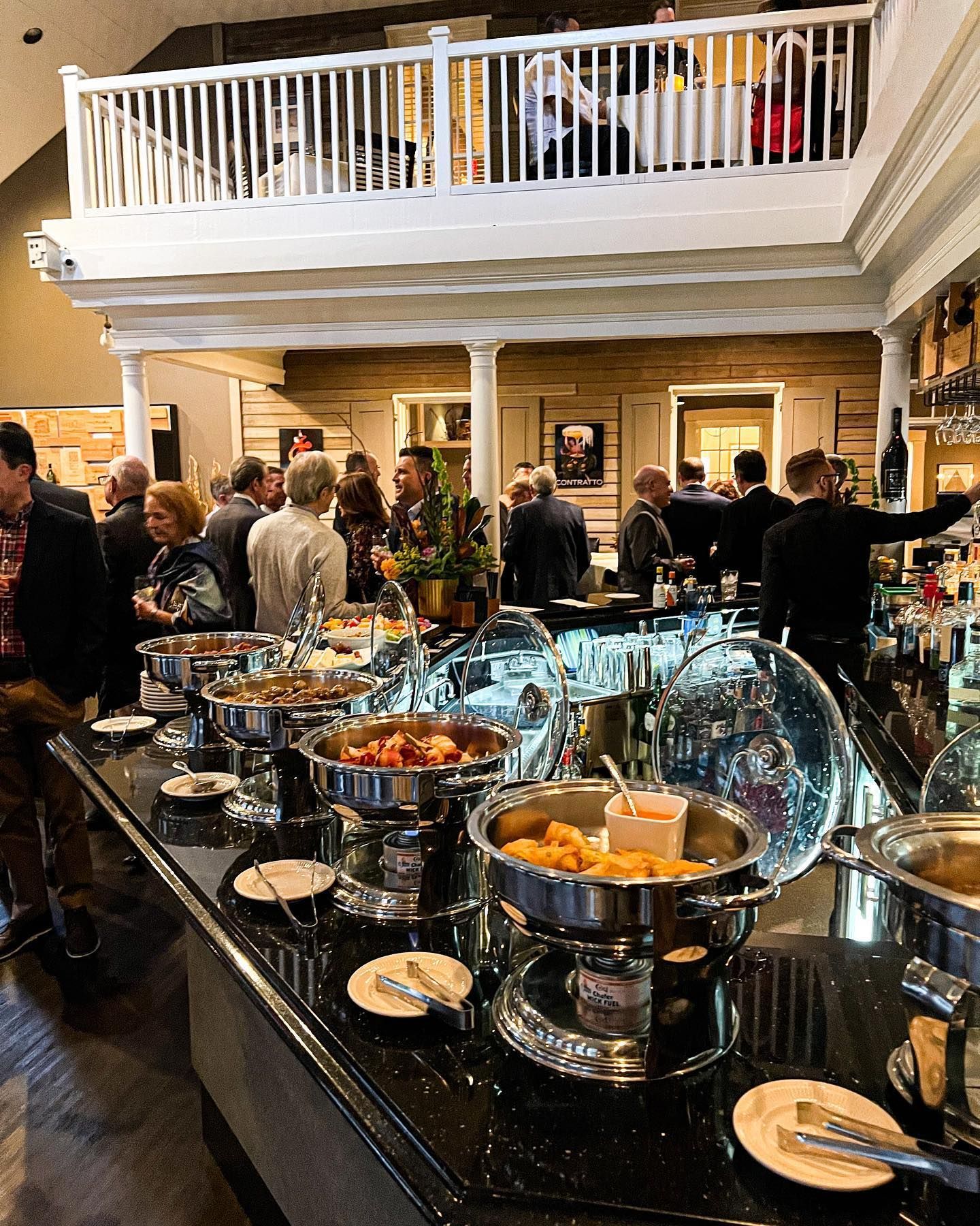 Buffet table with food and drinks in a crowded elegant lobby, with people gathered in the background