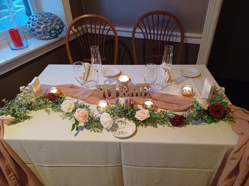 Elegant dining table with candles, floral garland, pink runner, and place settings by two chairs