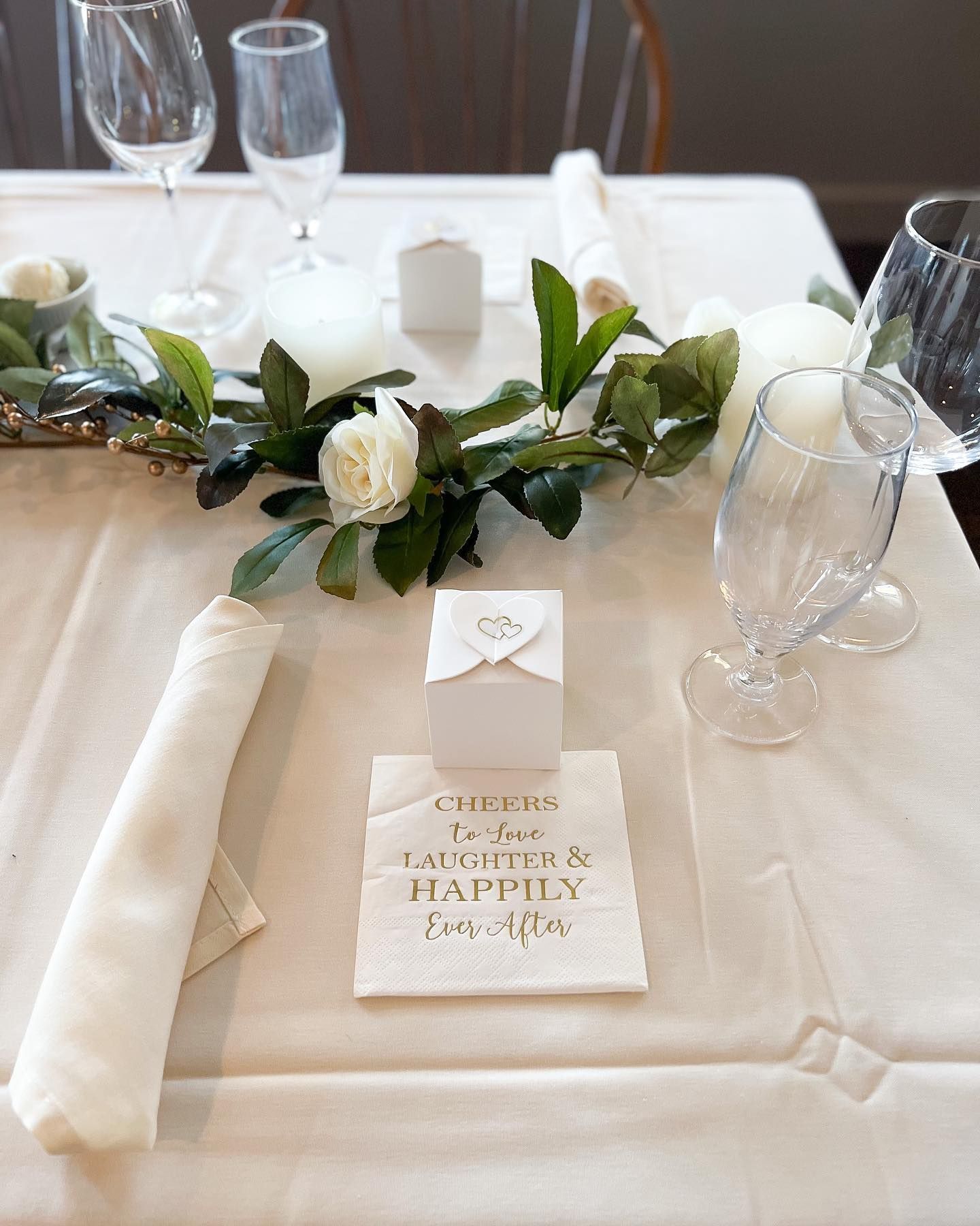 Elegant white wedding table setting with green floral centerpiece, candles, and personalized place card