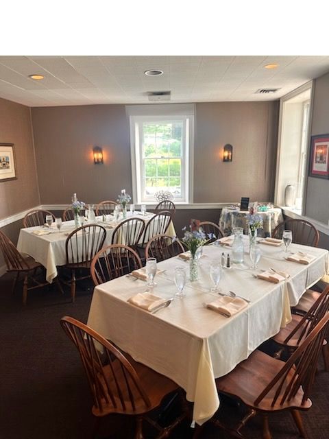 Elegant dining room with set white-tablecloth tables, wooden chairs, and soft wall sconces by a window