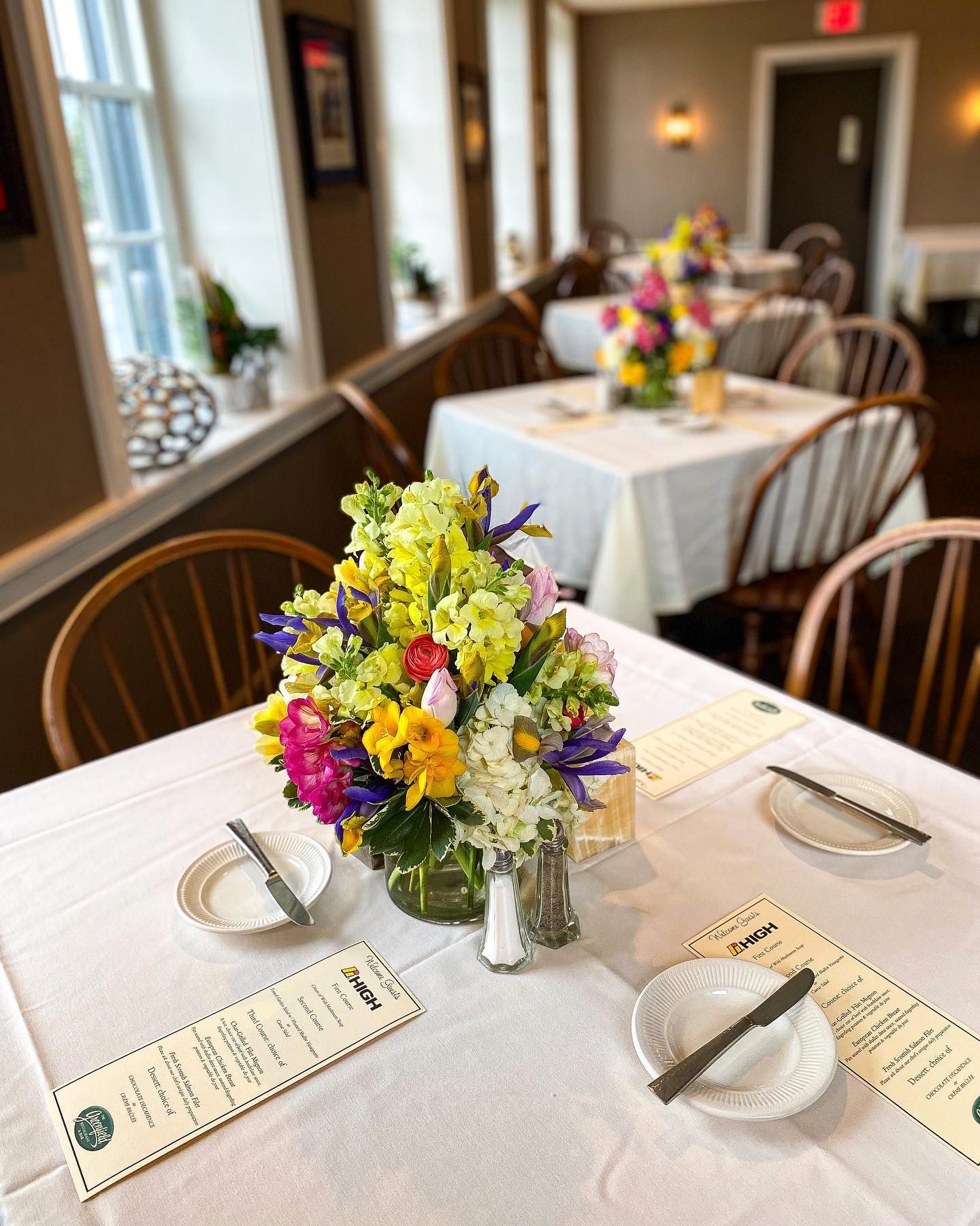 Flower centerpieces on set dining tables in a bright banquet room