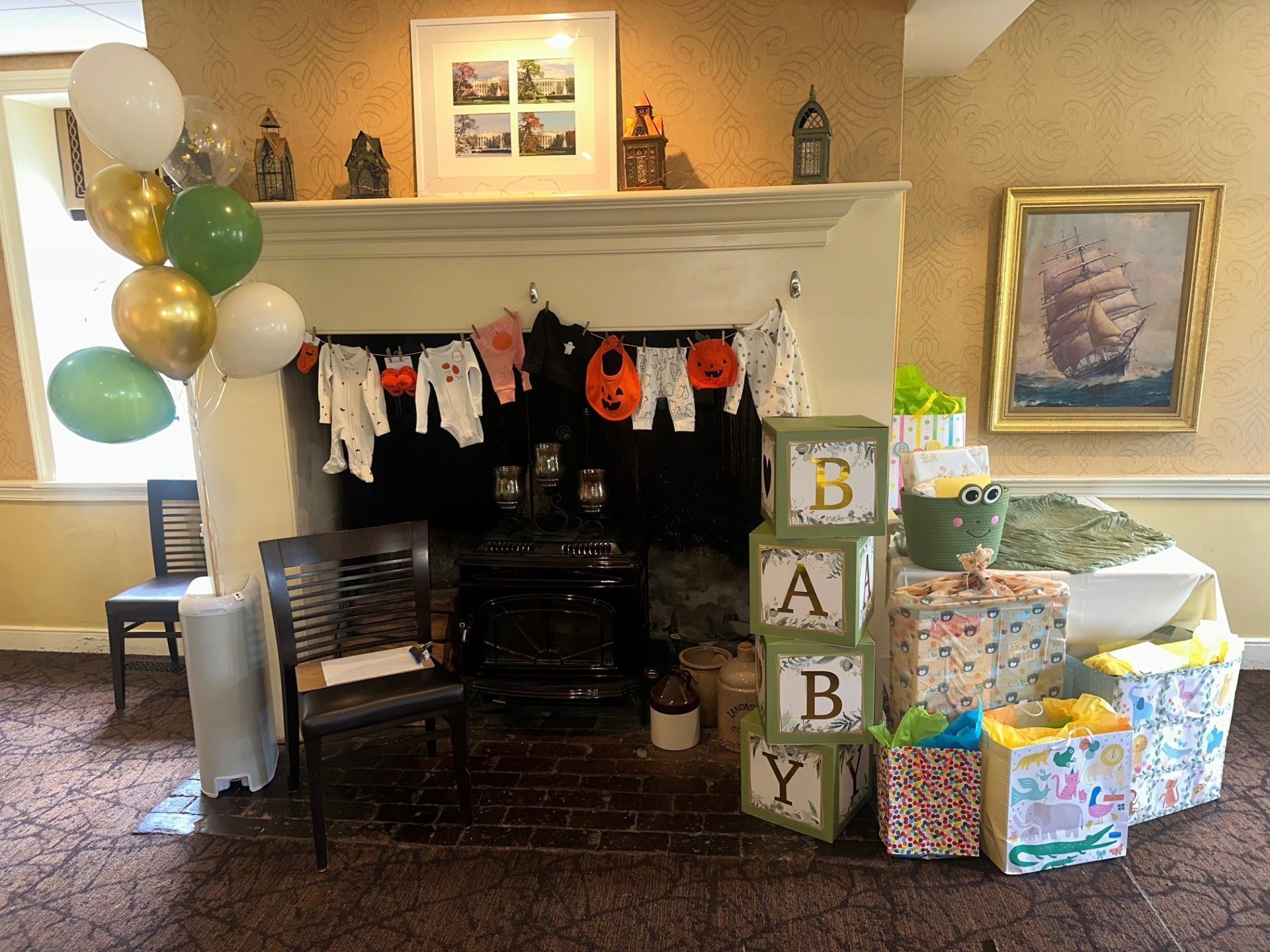 Decorated fireplace mantel with balloons, baby blocks, gifts, and hanging baby clothes in a cozy room