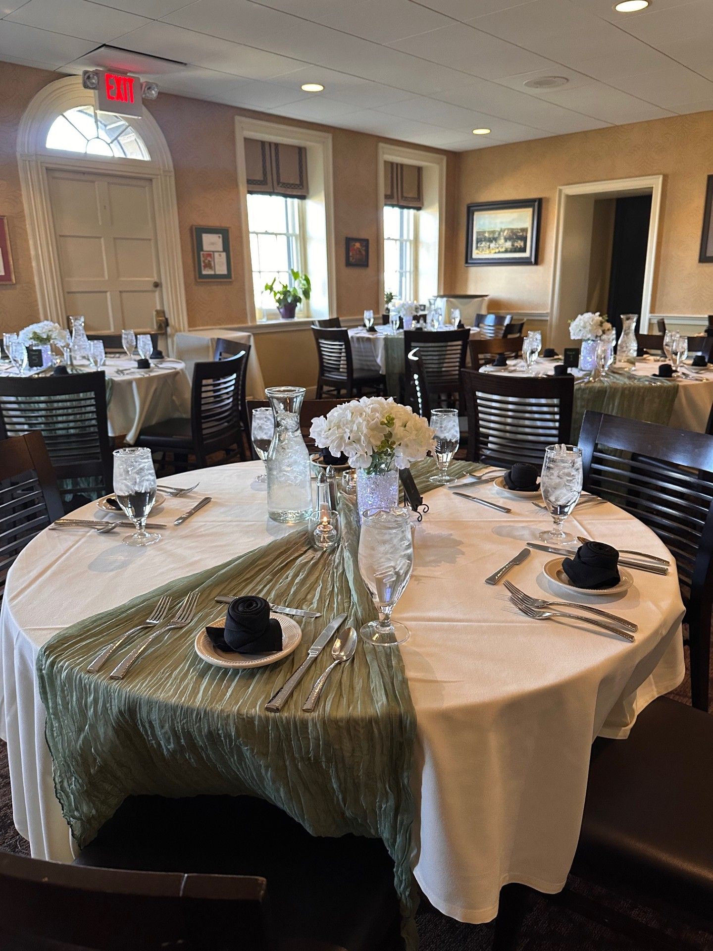Elegant banquet room with round, set tables, black chairs, and white floral centerpieces