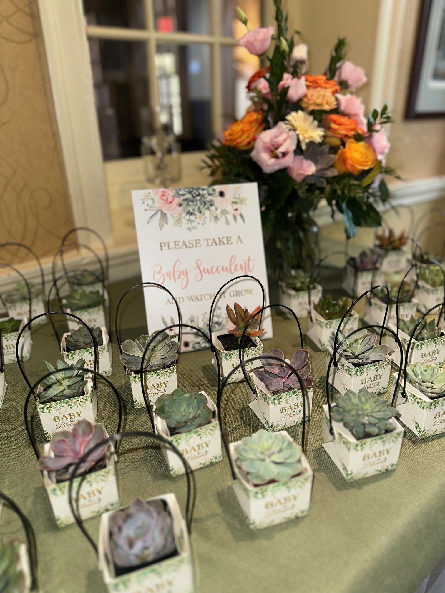 Flower-adorned favor boxes and a “Please take a baby shower favor” sign on a table