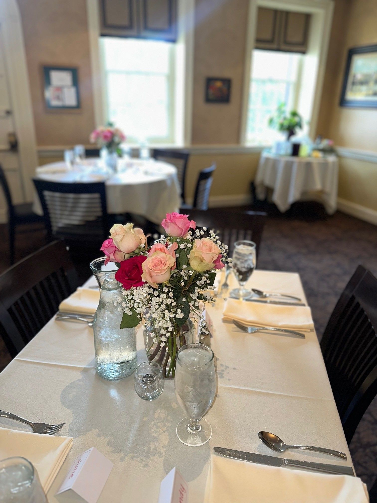 Floral centerpieces set on a white-clothed banquet table in a bright dining room