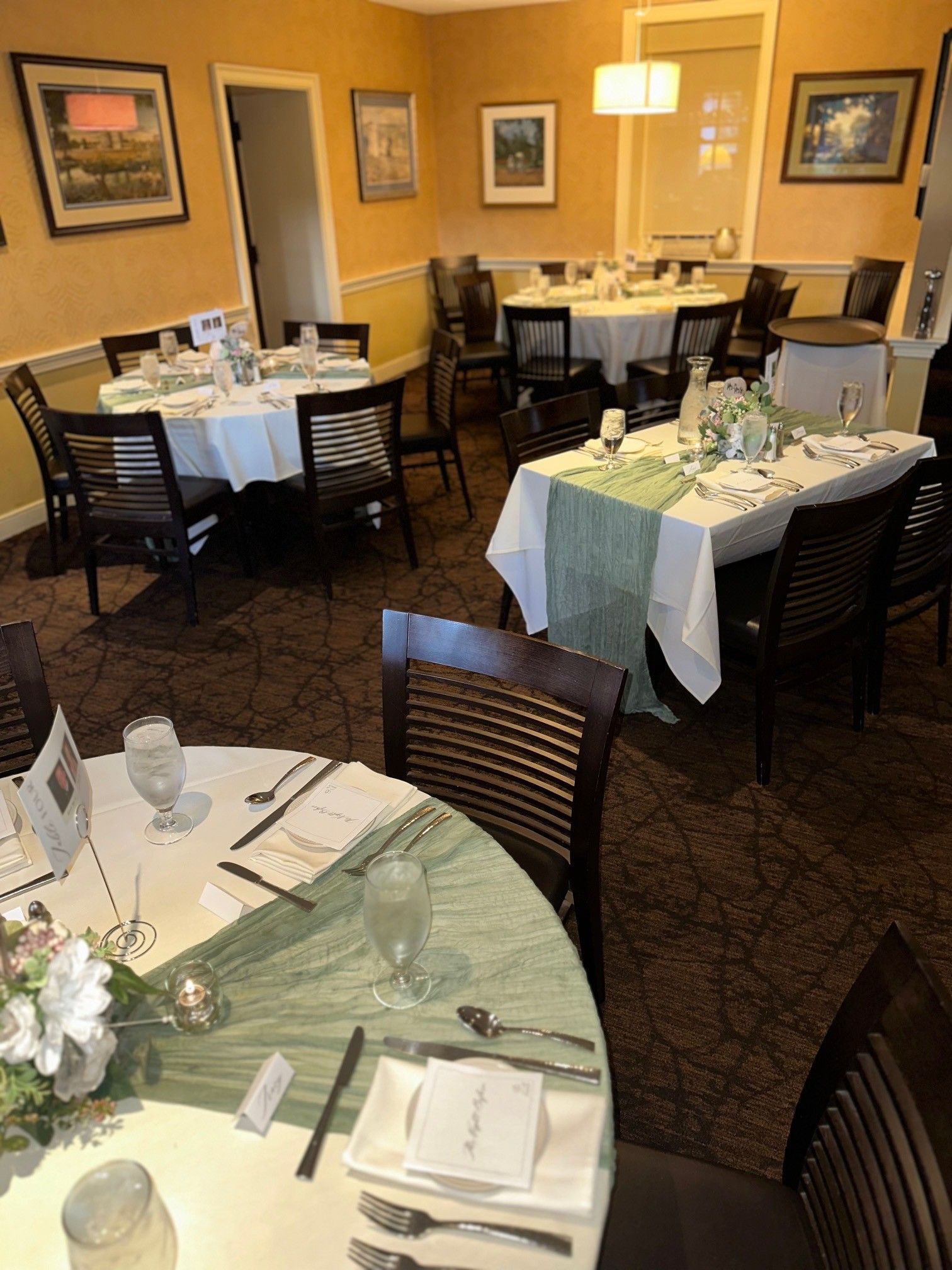 Empty restaurant dining room with set tables, white tablecloths, and warm yellow lighting
