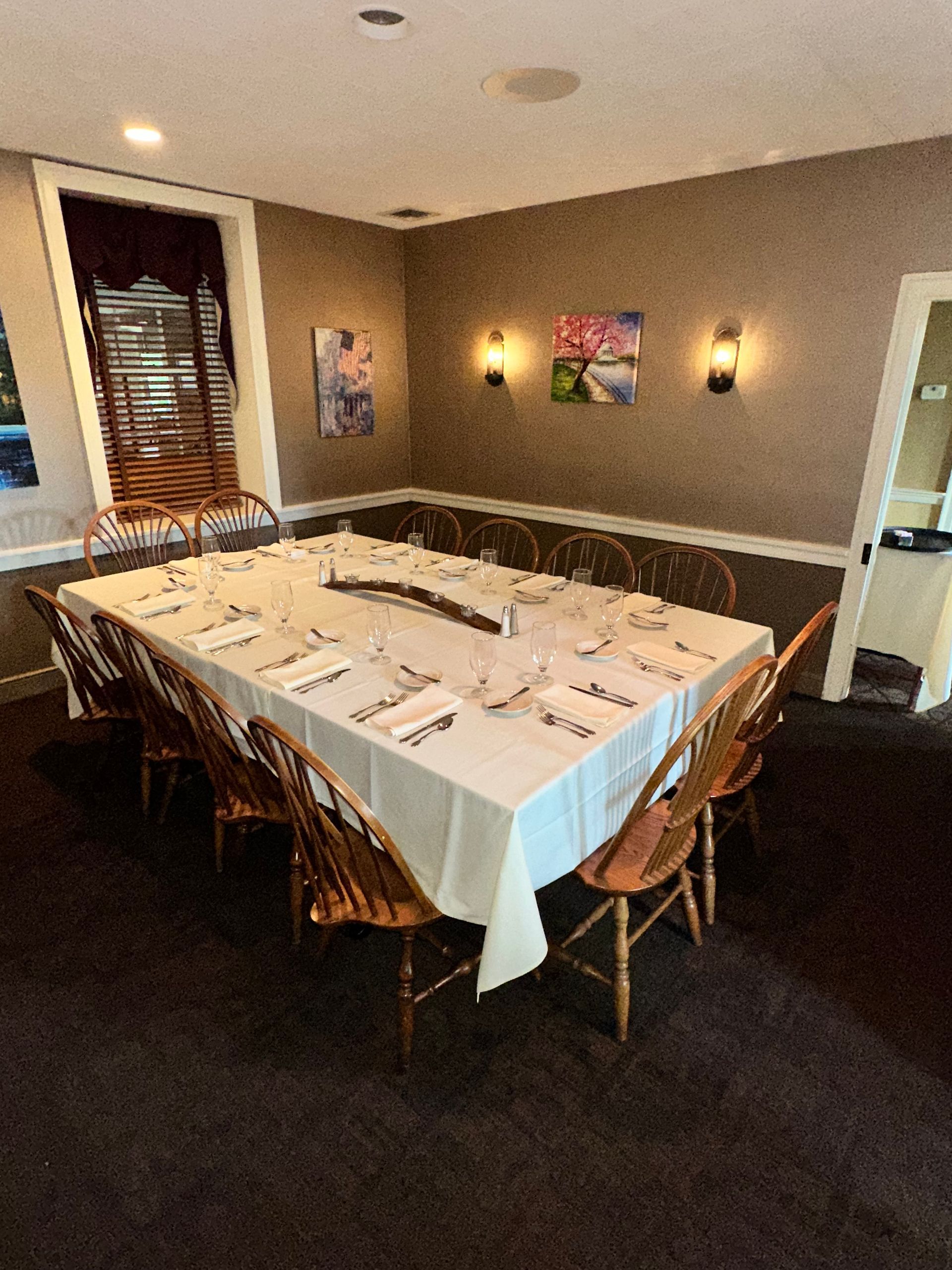 Dining room set for a formal meal, with a long white-clothed table and chairs in a cozy room
