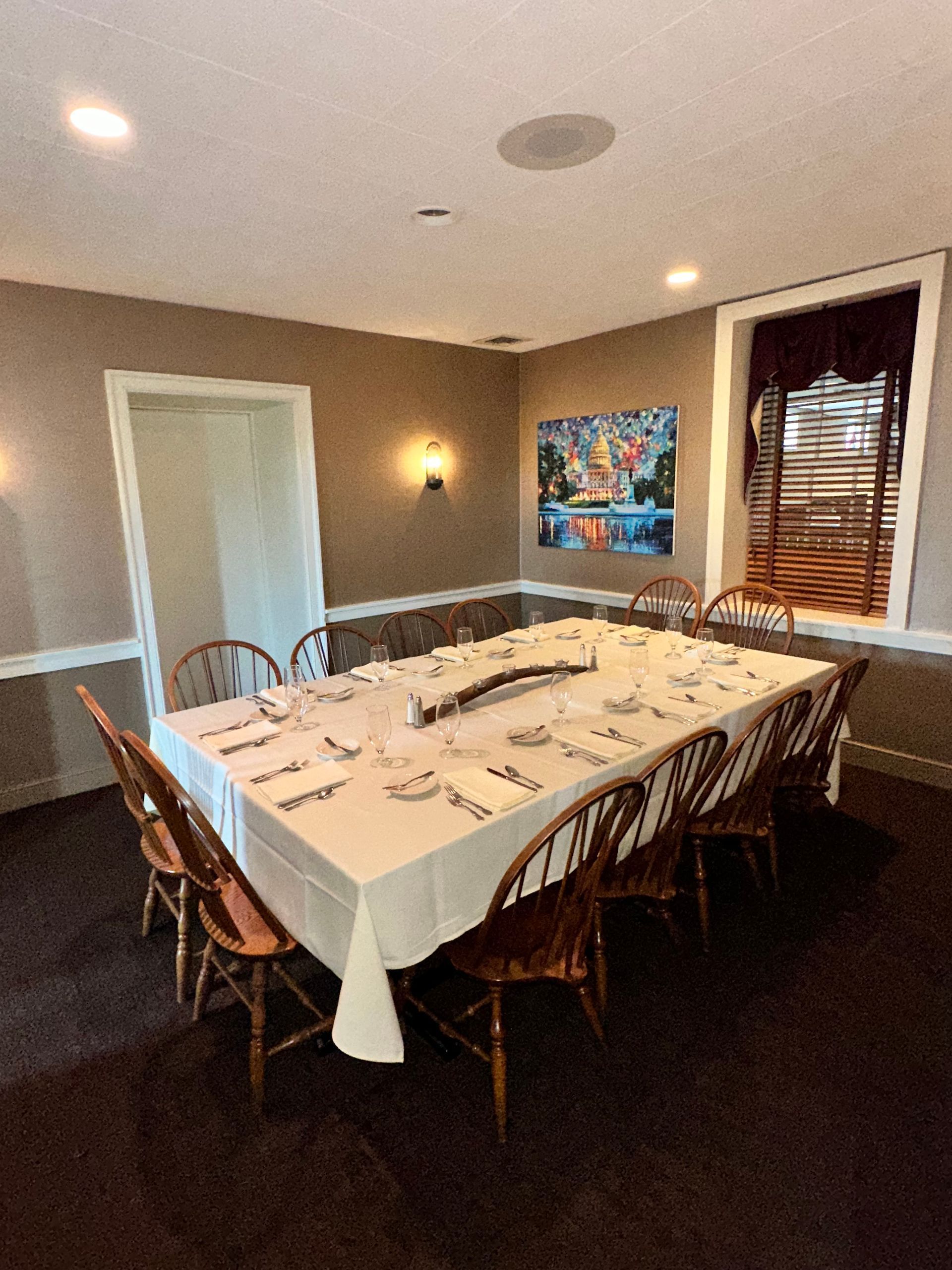 Set dining table in a warmly lit room with white tablecloth, candles, and chairs by a window and door