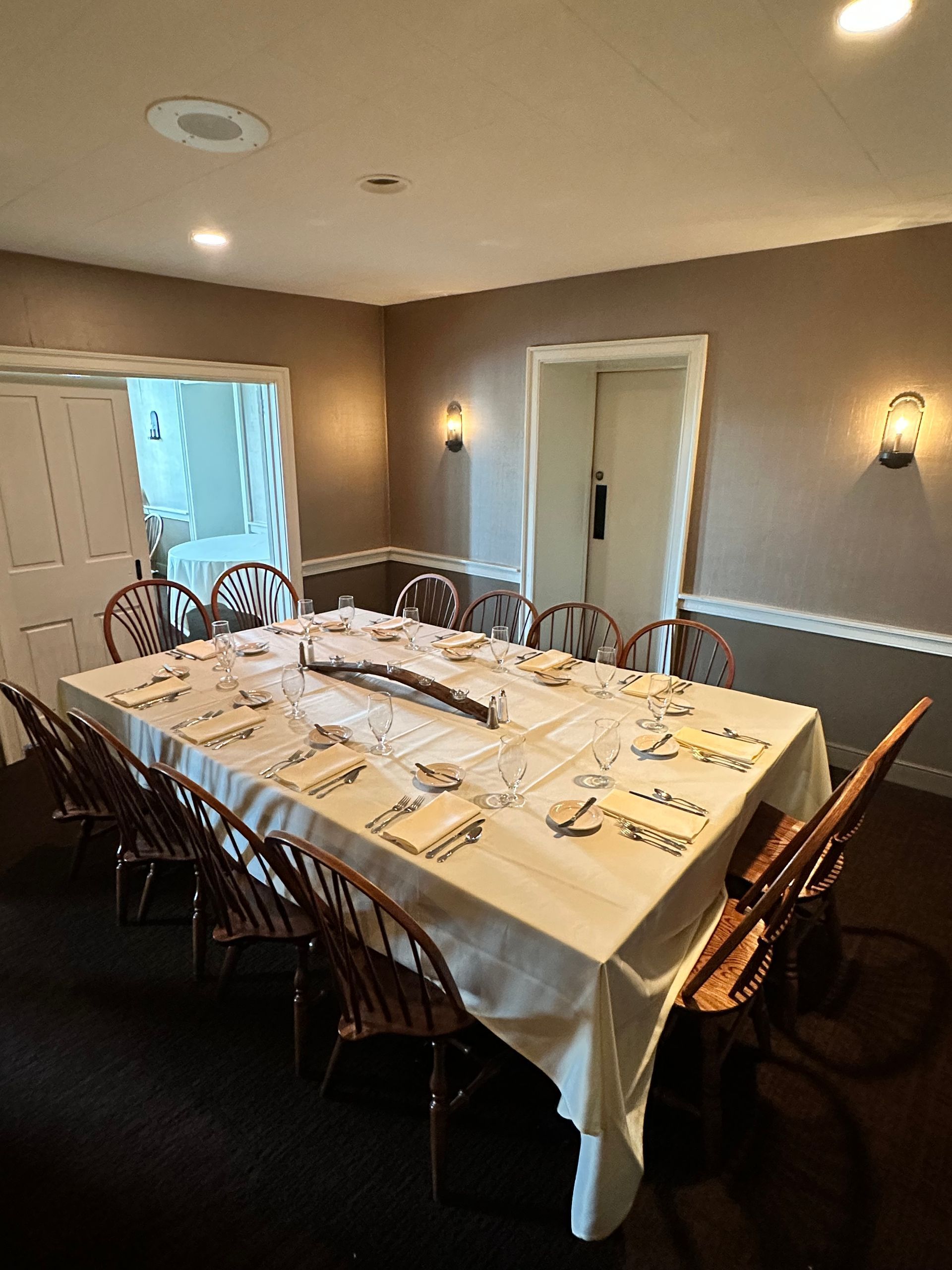 Set dining table in a warmly lit room with white tablecloth, chairs, and wall sconces