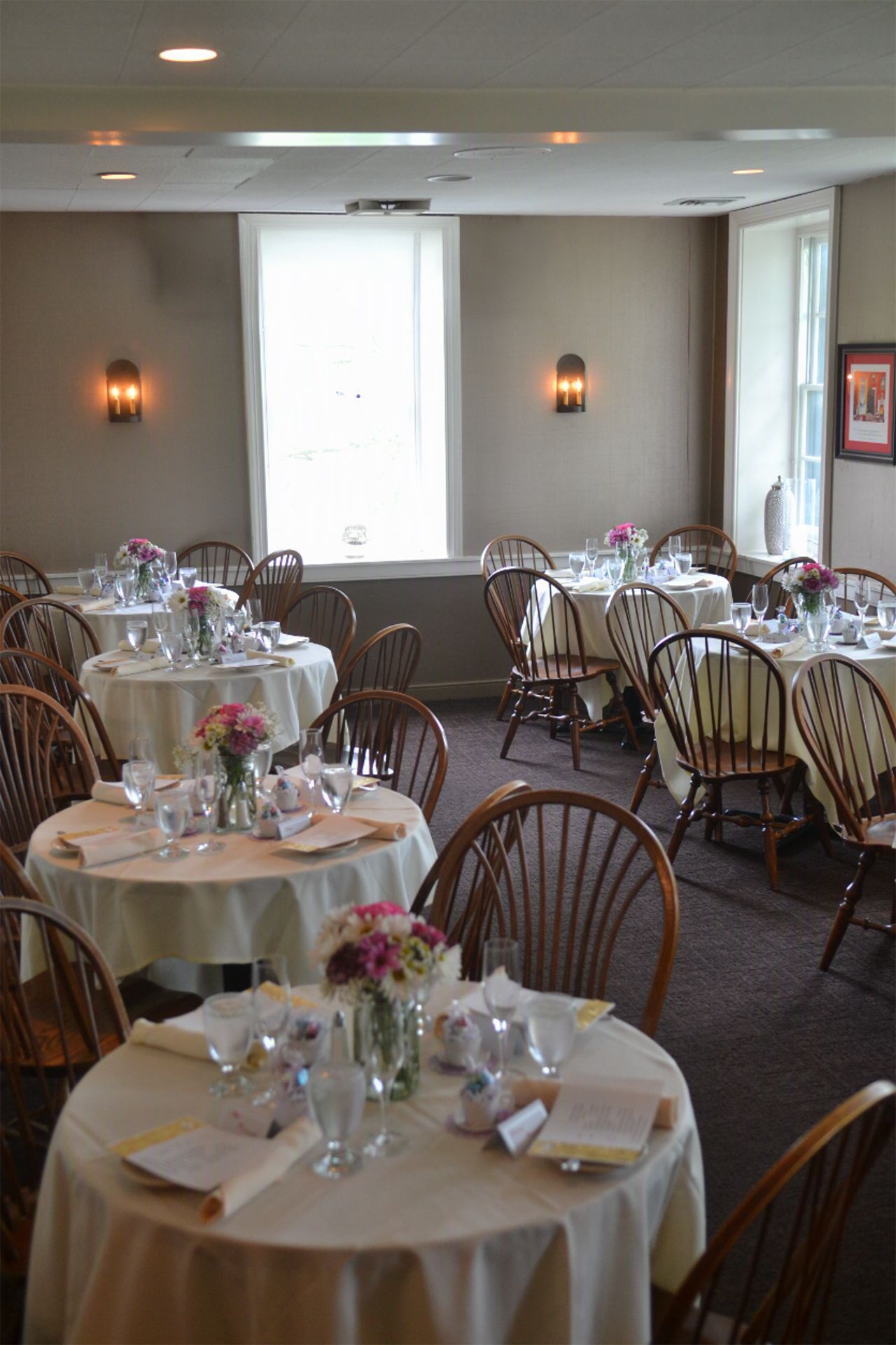 Banquet room with round tables set for dining, floral centerpieces, and chairs near a bright window