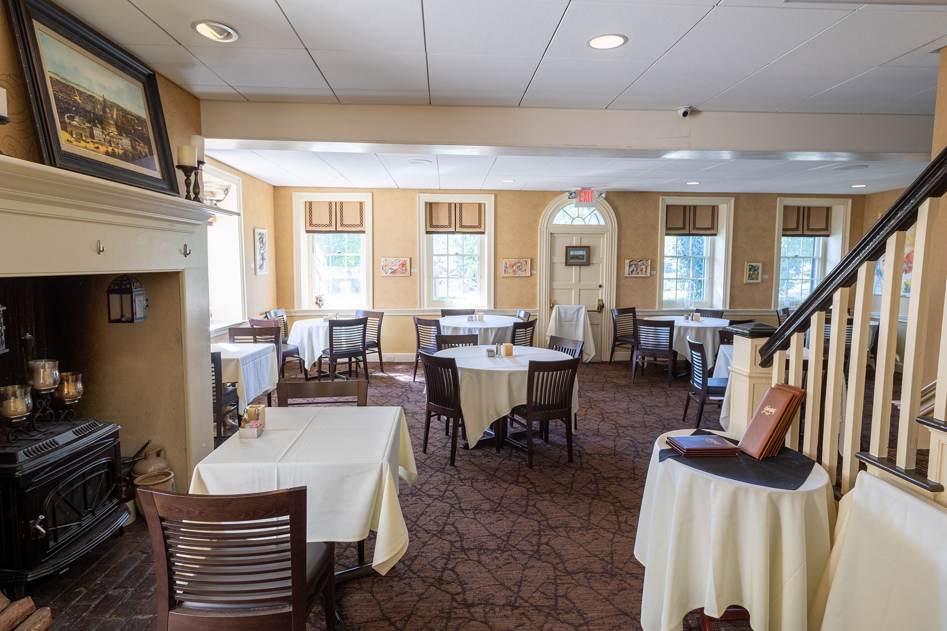 Elegant dining room with round tables, patterned carpet, and a staircase along the right wall