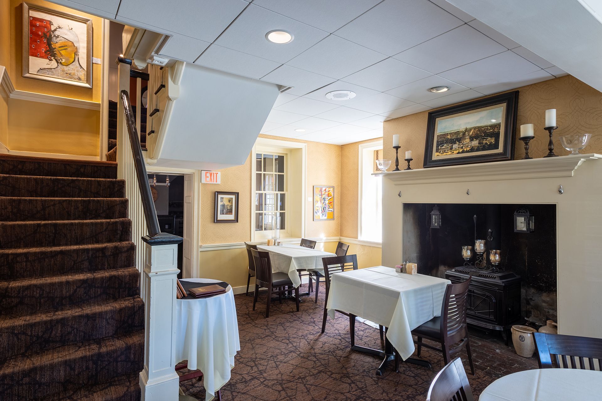Cozy restaurant dining room with set tables, carpeted stairs, and a large fireplace on the right