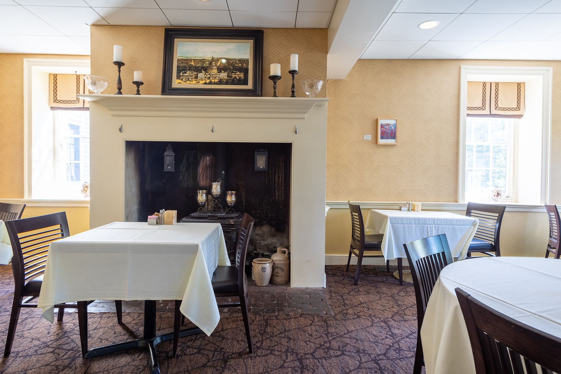 Dining room with tables set with white cloths and chairs around a central fireplace.