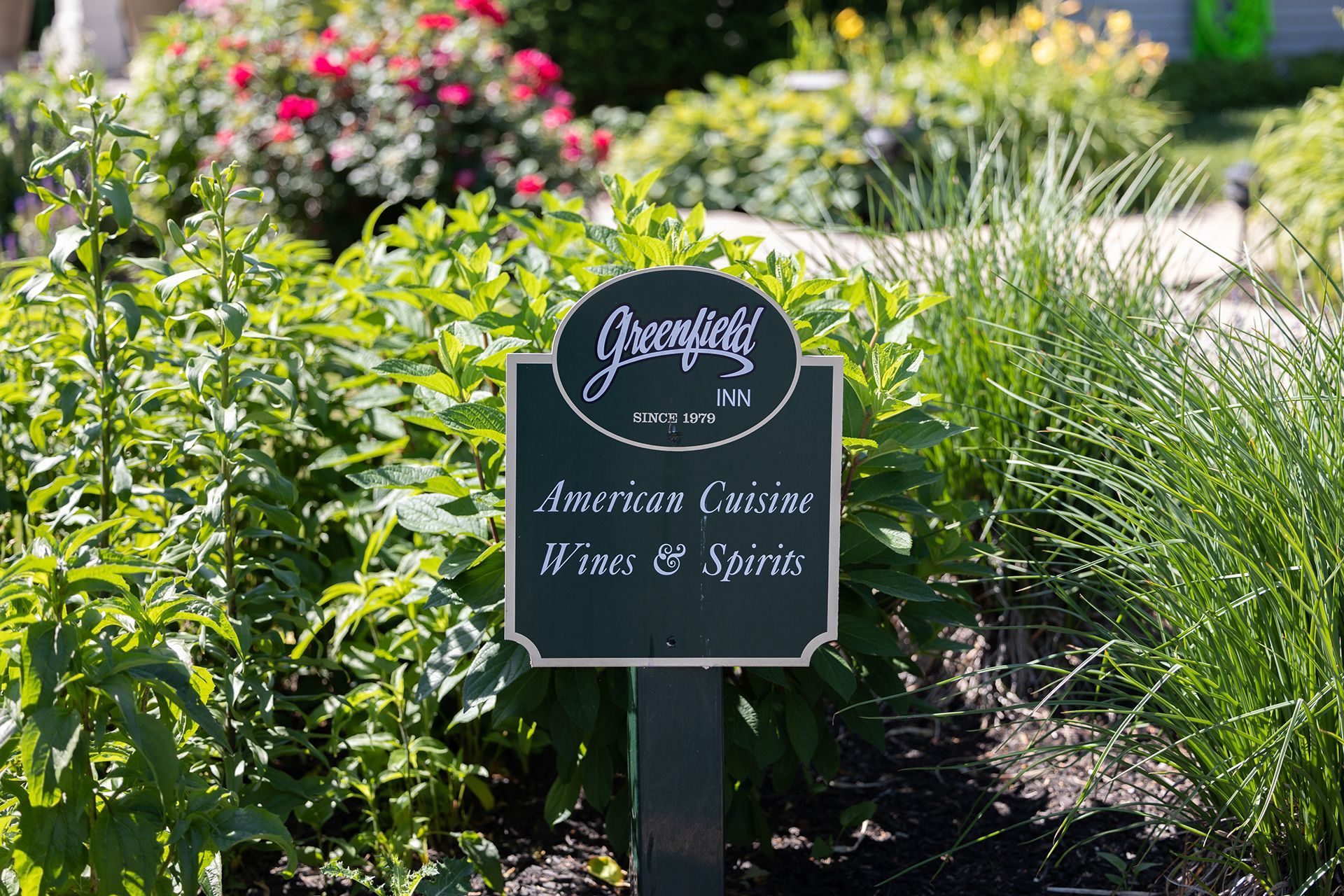 Garden sign among flowers reading 'Jacquelyn’s Fine Wines & Spirits.'