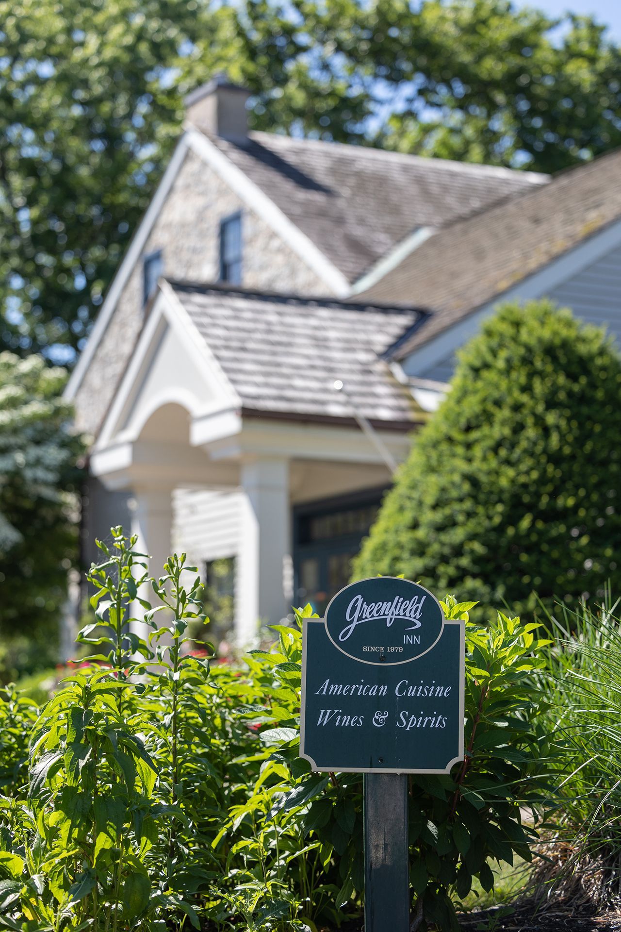 Black sign in front of a white house with green landscaping and blue sky