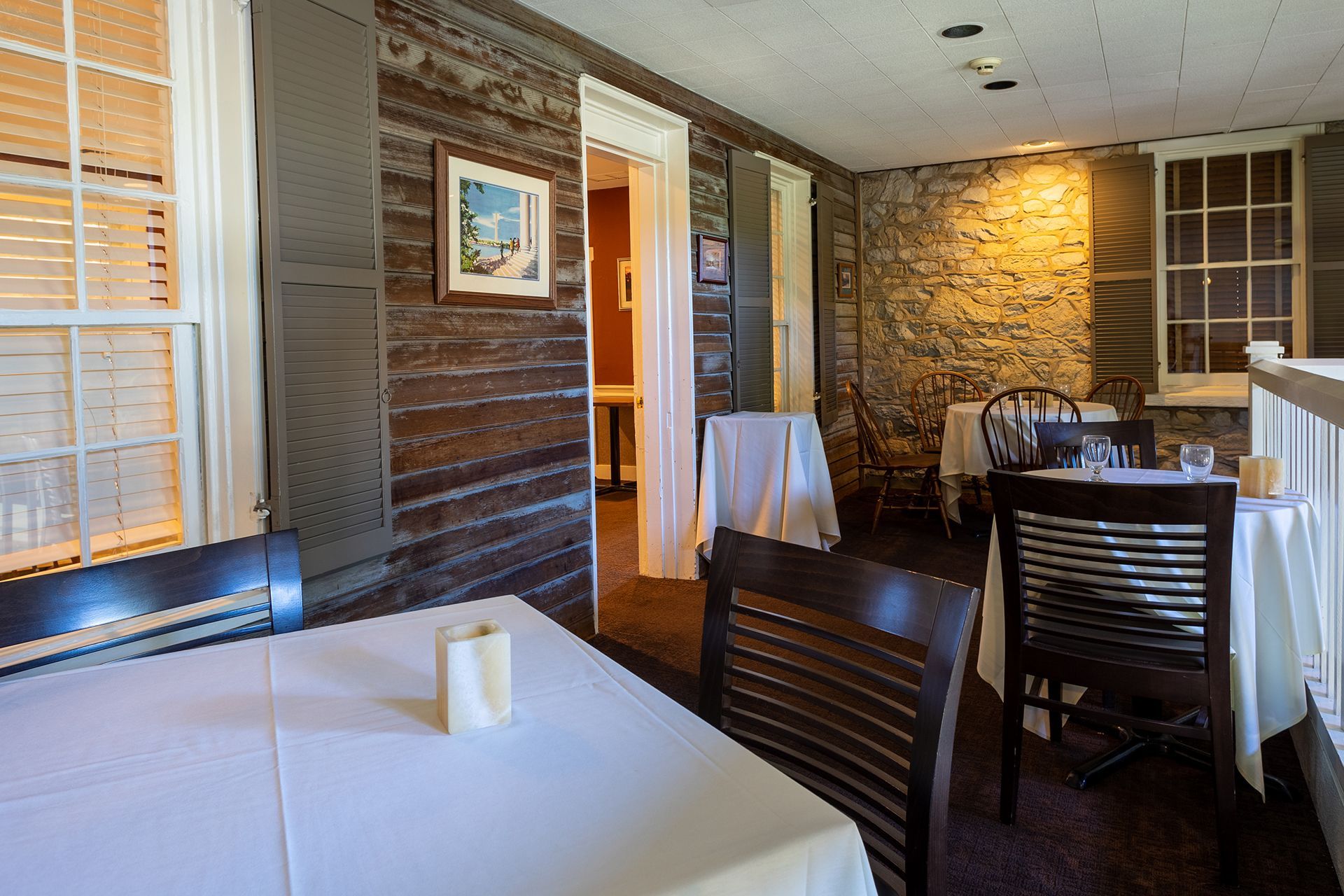 Restaurant dining room with white tablecloth tables, dark chairs, brick walls, and warm lighting
