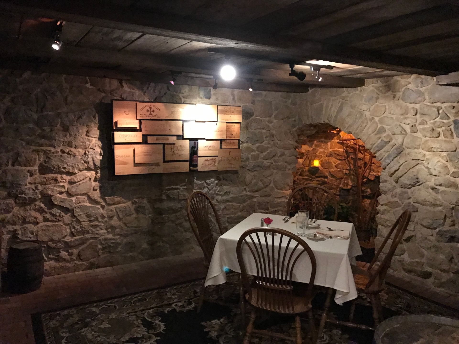 Stone-walled restaurant nook with a set dining table, wooden chairs, and warm wall lighting
