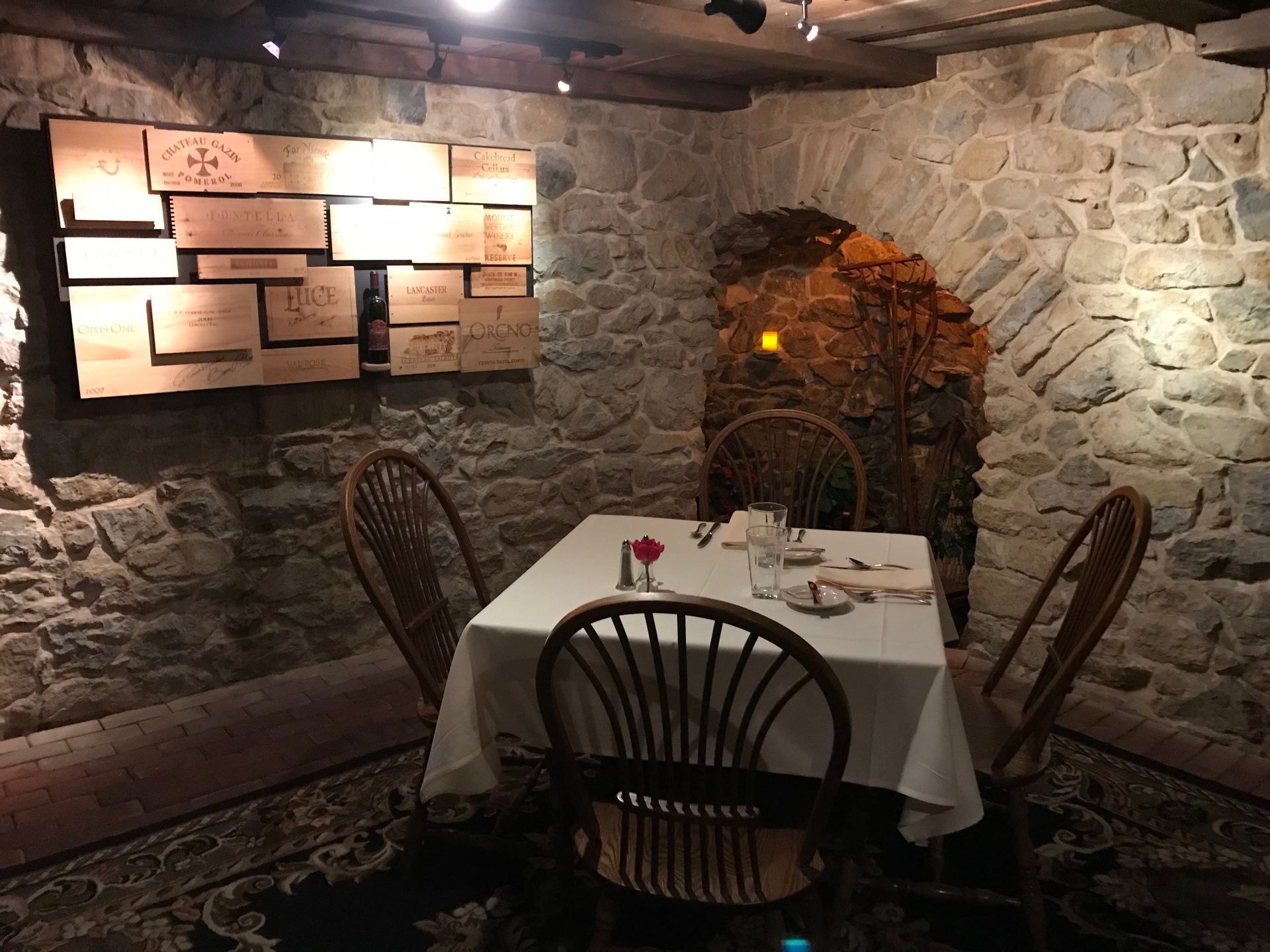 Cozy stone-walled restaurant nook with a white tablecloth table, chairs, and warm wall lights