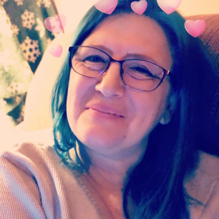 Woman with blue hair and glasses smiles; pink hearts overlay the image.