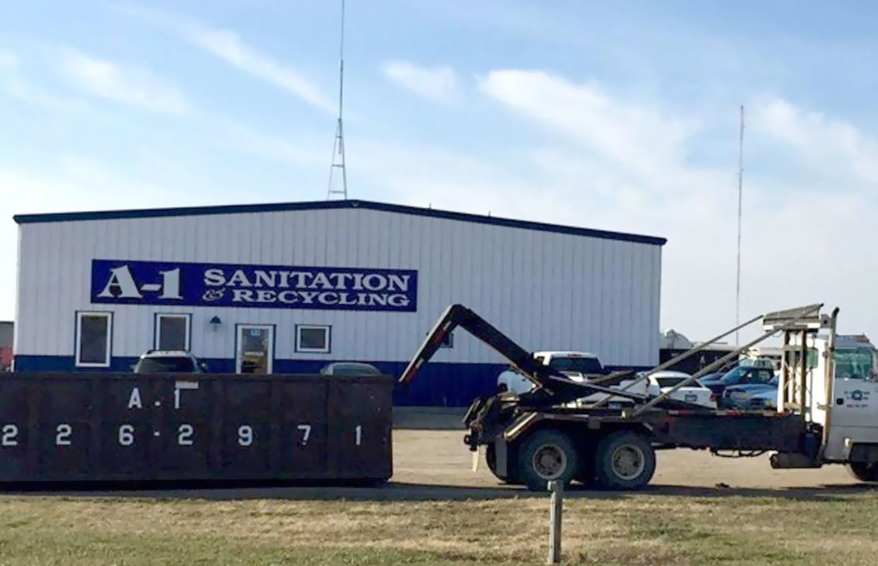 A-1 Sanitation & Recycling building with a truck lifting a large dumpster. Blue sky overhead.