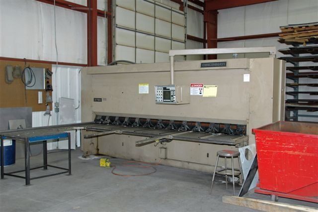 A large machine is sitting in a warehouse next to a red dumpster