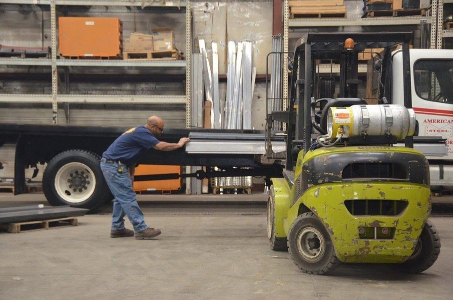 A man pushing a forklift in front of a truck