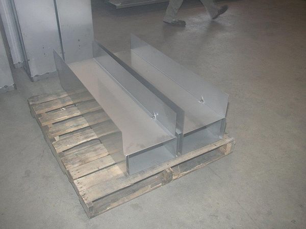 A person is standing next to a wooden pallet with metal pieces on it.