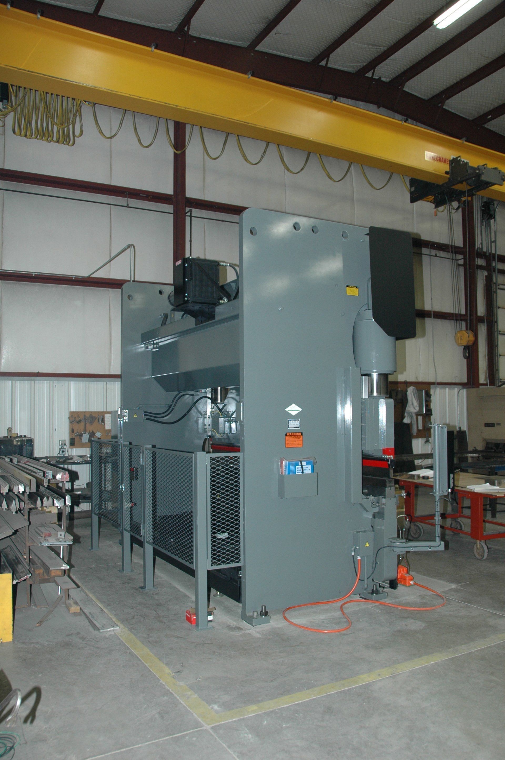 A large machine is sitting under a crane in a factory.