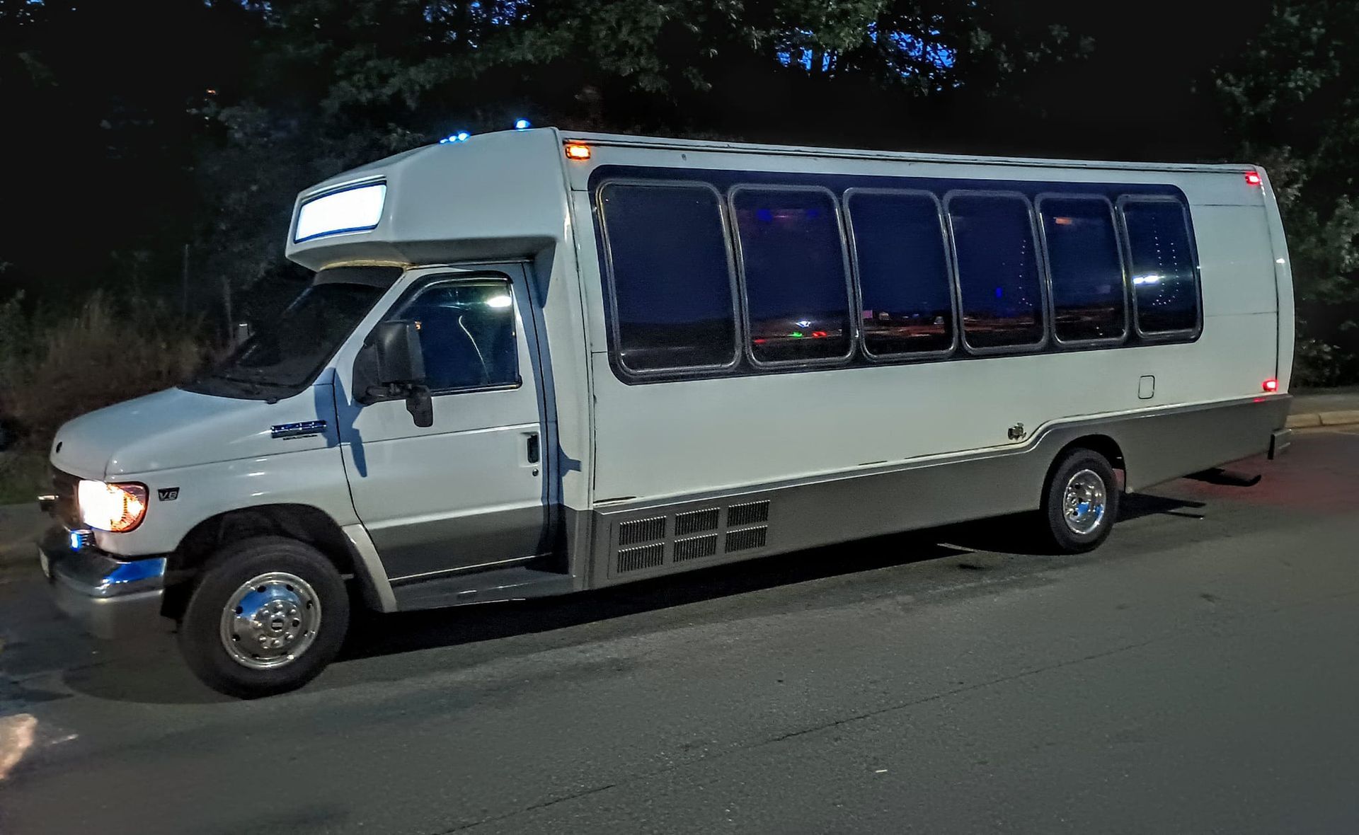A white party bus with tinted windows parked on a street at dusk.