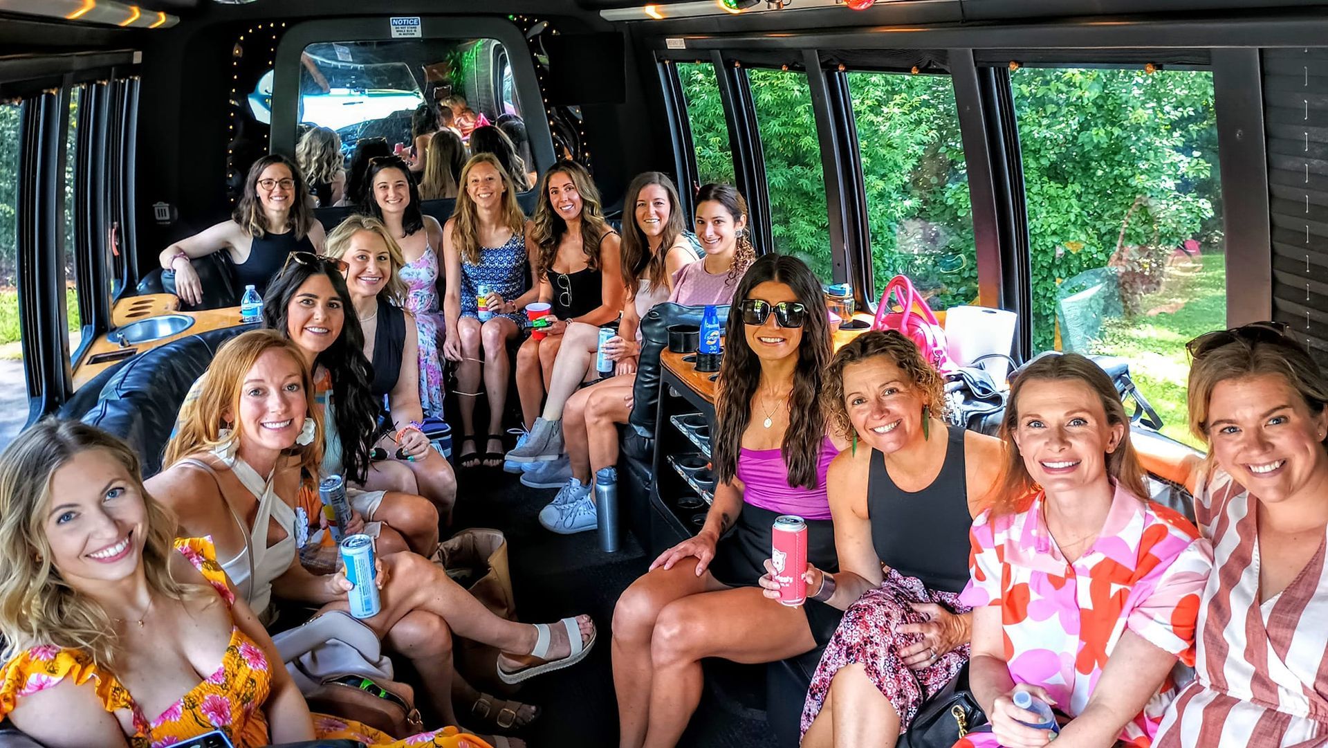 A group of people sitting inside a party bus, smiling and posing for a photo while holding drinks.