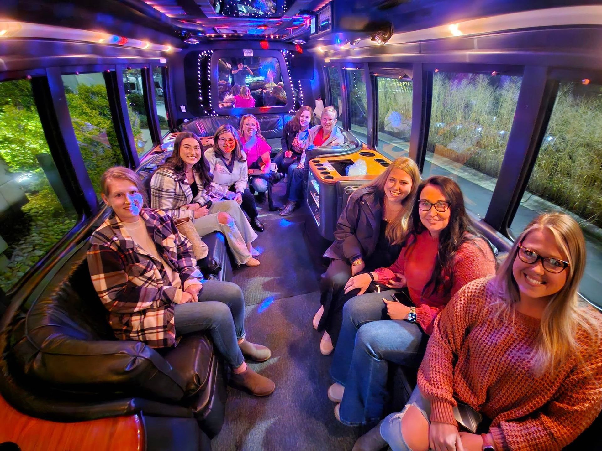 A group of people sitting inside a party bus with purple lighting, smiling and looking toward the camera.