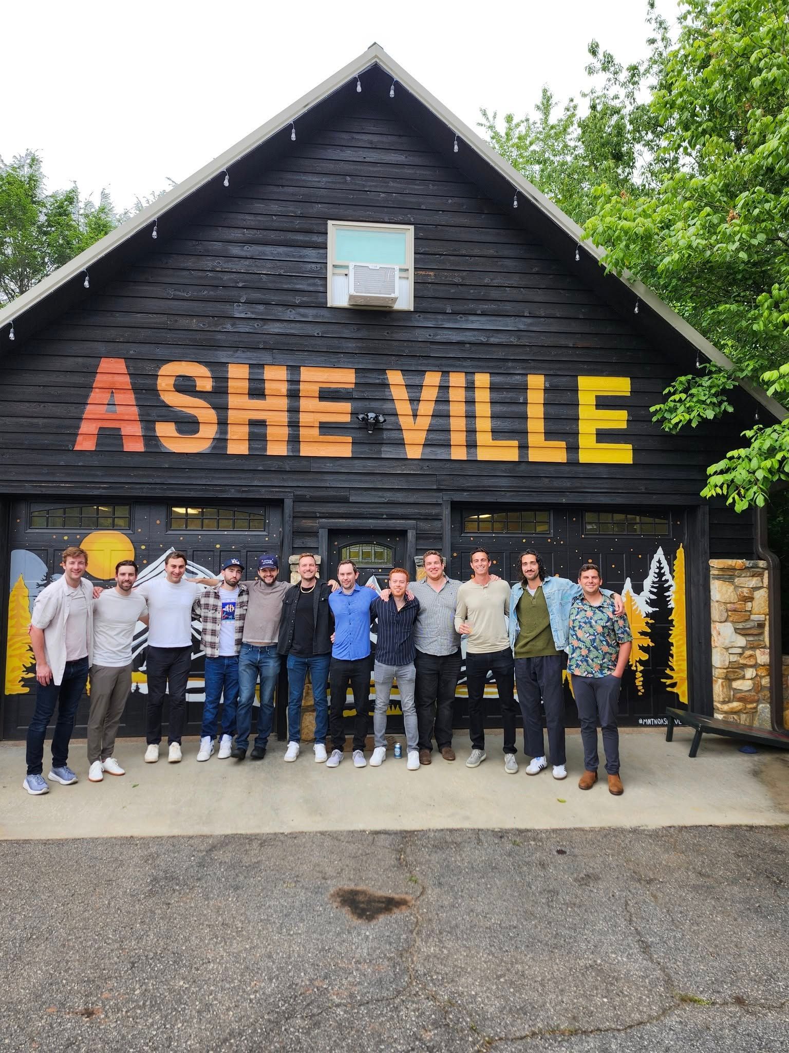 A group of fifteen people stand in front of a dark building with 