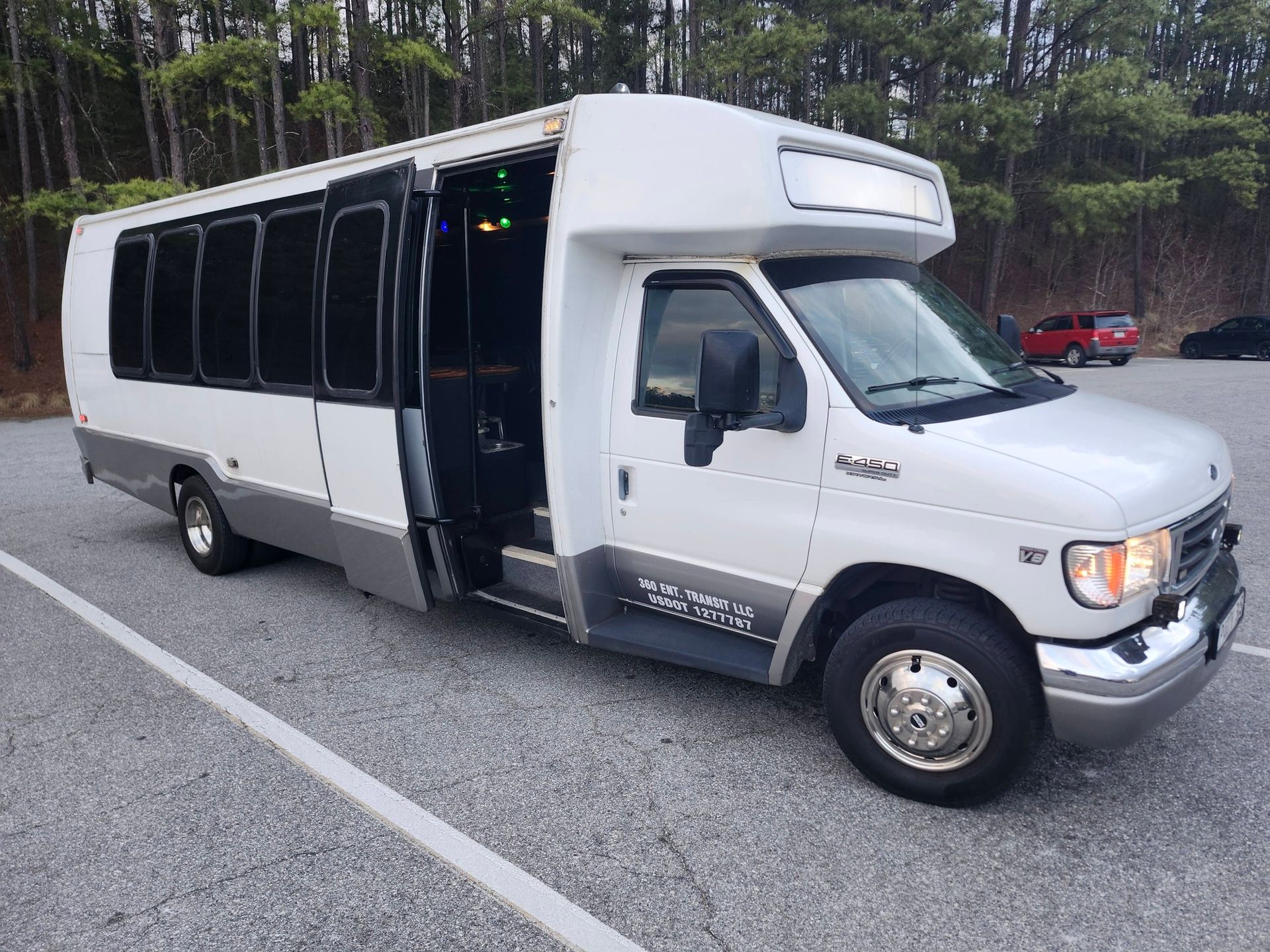 White passenger shuttle bus parked in a gravel lot with its passenger door open, viewed from the front quarter.
