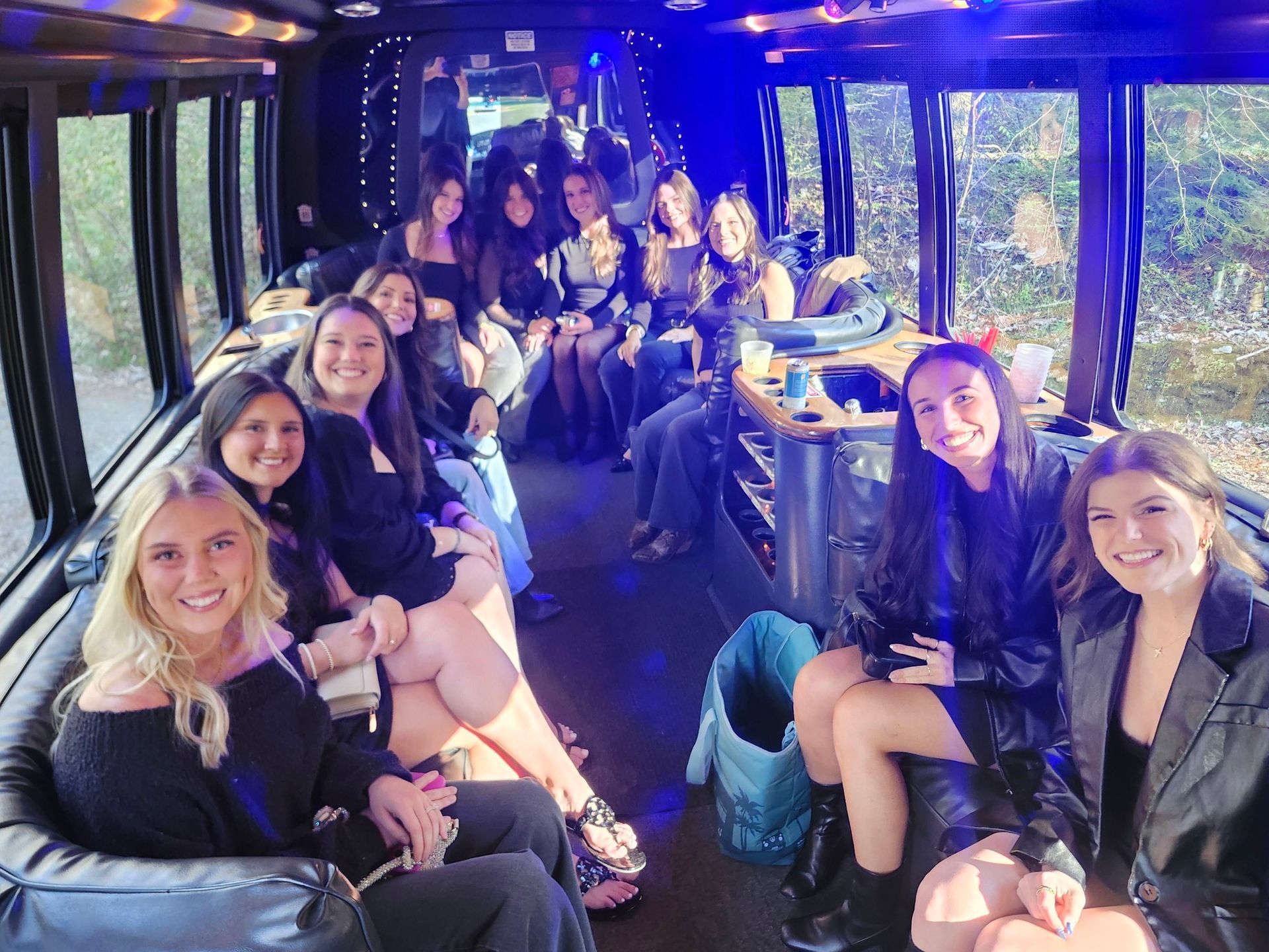 A group of people sitting inside a party bus with blue lighting, smiling and looking toward the camera.