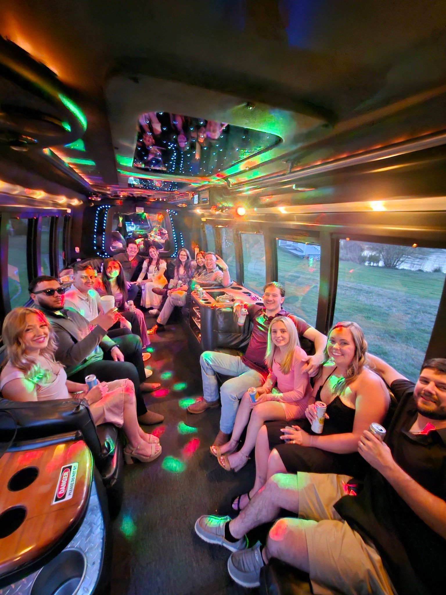 A group of people sitting inside a party bus with colorful lights, interior seating, and windows showing a dark exterior.
