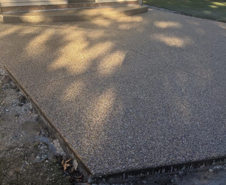 Exposed aggregate concrete patio with a step leading to a doorway, viewed from an outdoor ground-level angle.