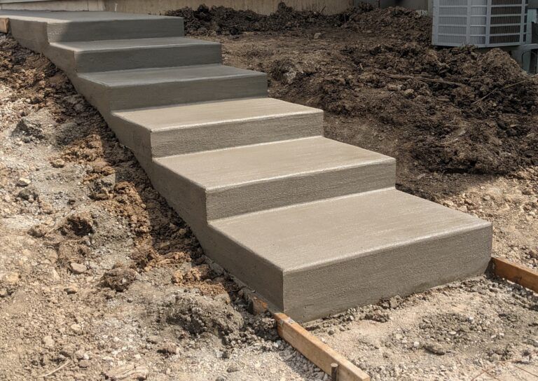 A set of newly poured concrete stairs outdoors on a dirt slope, with wooden forms visible at the base.