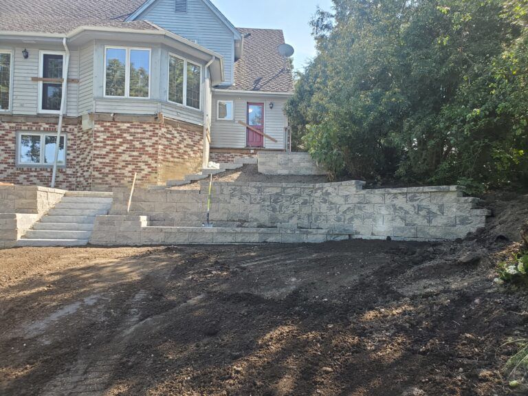 A two-story house with a newly constructed stone retaining wall and concrete steps leading to the back entrance.